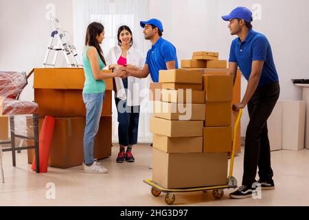 Les filles adultes se secouant les mains avec le garçon de livraison alors que les boîtes de carton sont prêtes à se déplacer Banque D'Images