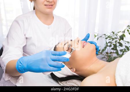 Salon de beauté, docteur en gants bleus faisant des procédures dermatologiques avec ultra sonique scaber à une belle femme. Banque D'Images