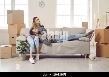 Un jeune couple heureux prend une pause et s'assoit sur un canapé tout en déménagent dans leur nouvelle maison Banque D'Images