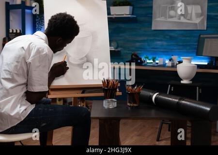 Jeune peintre esquissant vase faire des ombres à l'aide d'un crayon graphique professionnel travaillant à l'ilustration créative pour la leçon d'art.Homme concentré étudiant dessin sur toile peinture dessin artistique Banque D'Images