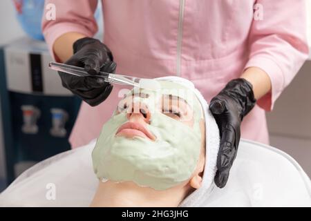 Application du masque vert clair avec la brosse dans le traitement de spa médecine alternative.Masque de gommage du visage, soins de beauté spa, soins de la peau. Banque D'Images