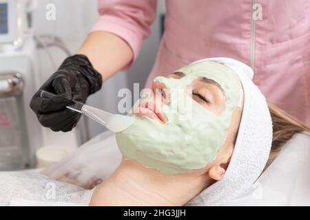 Application du masque vert clair avec la brosse dans le traitement de spa médecine alternative.Masque de gommage du visage, soins de beauté spa, soins de la peau. Banque D'Images