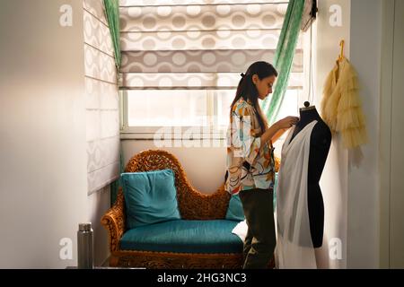 Une jeune femme debout tout en mettant sa tenue sur un mannequin avec un canapé derrière. Banque D'Images