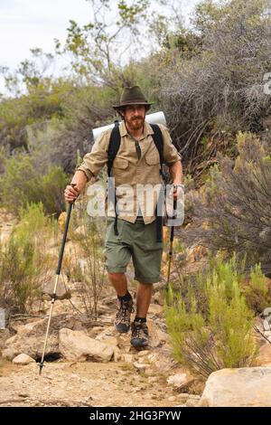 Pleine longueur de jeune homme barbu de randonnée caucasienne avec des bâtons parmi les plantes dans la forêt Banque D'Images