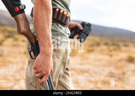 Section médiane de jeune chasseur tenant une carabine et des jumelles en forêt Banque D'Images