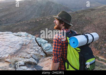 Jeune homme à barbe randonneur caucasien avec sac à dos portant un chapeau au sommet de la montagne Banque D'Images