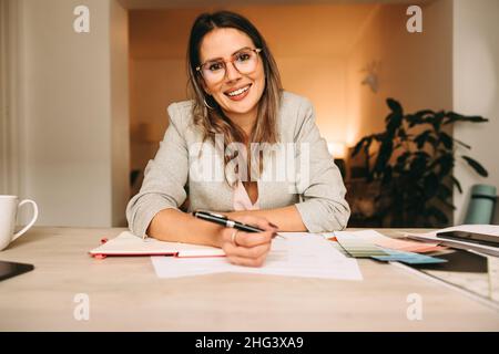 Joyeuse décoratrice d'intérieur assistant à une réunion en ligne avec ses clients.Bonne femme de créateur prenant des notes pendant un appel vidéo.Femme créative Banque D'Images