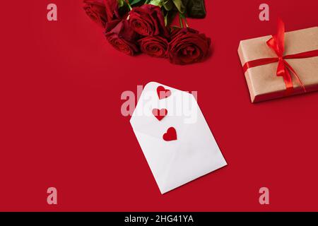 enveloppe avec valentines, boîte-cadeau et roses sur fond rouge. Banque D'Images