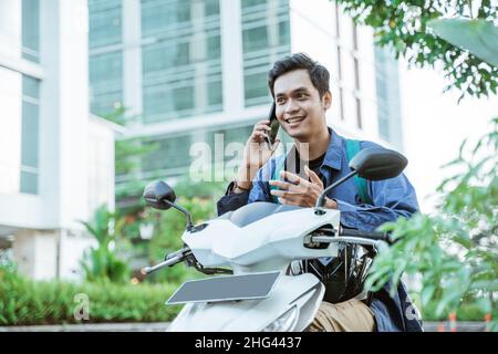 Homme asiatique appelant à l'aide d'un téléphone portable tout en conduisant une moto Banque D'Images