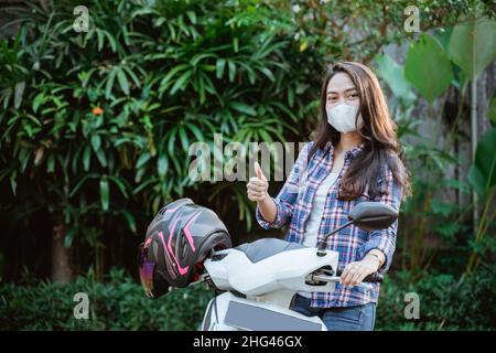 Belle fille debout portant un masque avec les pouces à côté de moto Banque D'Images