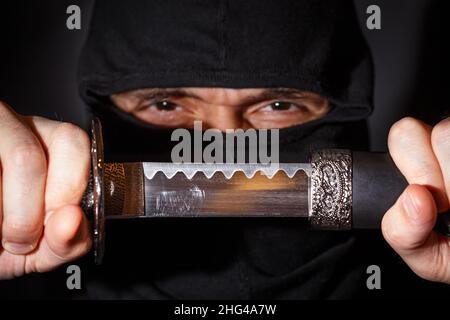 Ninja prêt à combattre, tenant une épée japonaise.Photo d'un guerrier vêtu de vêtements noirs et d'un visage fermé Banque D'Images