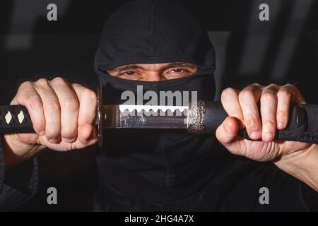 Ninja prêt à combattre, tenant une épée japonaise.Photo d'un guerrier vêtu de vêtements noirs et d'un visage fermé Banque D'Images