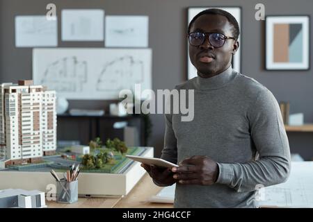 Ingénieur professionnel de l'ethnie africaine défilant en tablette tout en étant debout au bureau et à la recherche de croquis en ligne Banque D'Images