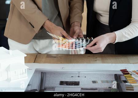 Mains de deux designers d'intérieur choisissant la couleur pour les murs d'appartement tout en se tenant par table avec plan et photos Banque D'Images