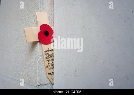 Un coquelicot artificiel sur une croix se dresse devant les inscriptions portant les noms des soldats tombés à la porte Menin d'Ypres, en Belgique. Banque D'Images