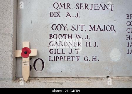 Un coquelicot artificiel sur une croix se dresse devant les inscriptions portant les noms des soldats tombés à la porte Menin d'Ypres, en Belgique. Banque D'Images