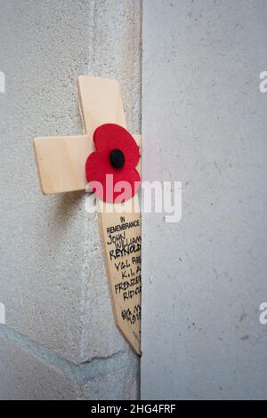 Un coquelicot artificiel sur une croix se dresse devant les inscriptions portant les noms des soldats tombés à la porte Menin d'Ypres, en Belgique. Banque D'Images