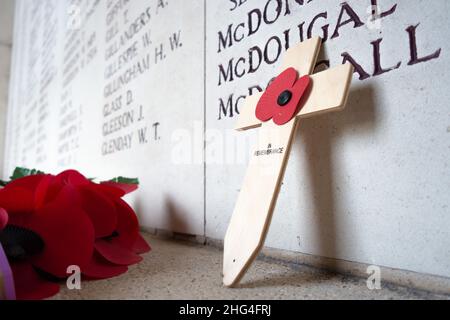 Un coquelicot artificiel sur une croix se dresse devant les inscriptions portant les noms des soldats tombés à la porte Menin d'Ypres, en Belgique. Banque D'Images