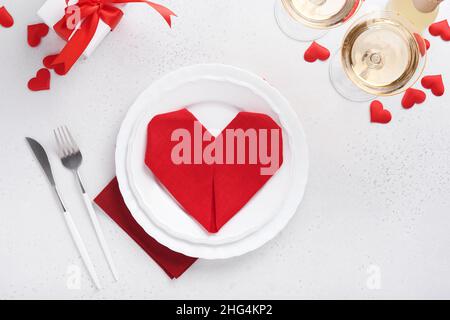 Table de jour de Valentinas couleur blanche avec argenterie blanche, serviette rouge pliée comme coeur, bougies, champagne, verres sur fond blanc pour greeti Banque D'Images