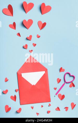 Enveloppe en papier rouge avec une note blanche à l'intérieur d'un stylo et coeurs en papier sur fond bleu.Lettre d'amour Valentin concept. Banque D'Images