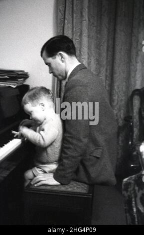 1950s, historique, un père assis derrière son jeune fils qui est assis sur un tabouret jouant des clés sur un piano, Angleterre, Royaume-Uni. Banque D'Images