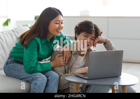 Un jeune couple asiatique plein d'amour utilisant un ordinateur portable, regardant des vidéos ou des films, magasiner à distance, consulter les réseaux sociaux en ligne Banque D'Images