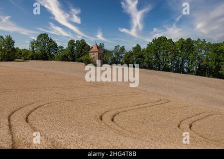 Ancienne tour de pierre dans un champ d'orge avec des lignes courbes à motifs en Dordogne France Banque D'Images