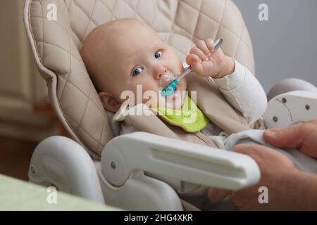 Bébé mange du fromage cottage assis dans une chaise d'enfant Banque D'Images