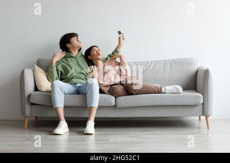 Couple asiatique du millénaire en train d'allumer la climatisation, à l'aide de la télécommande, souffrant de la chaleur estivale à la maison, mockup Banque D'Images