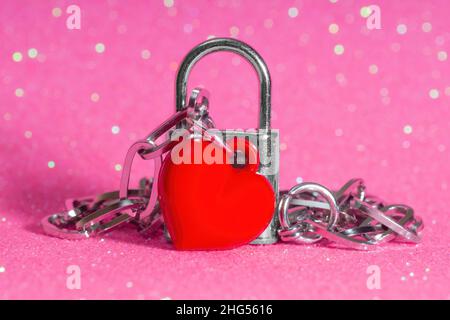 Pendentif en forme de coeur rouge attaché à un petit cadenas sur un fond rose étincelant.Symbole de l'amour vrai et infini. Banque D'Images