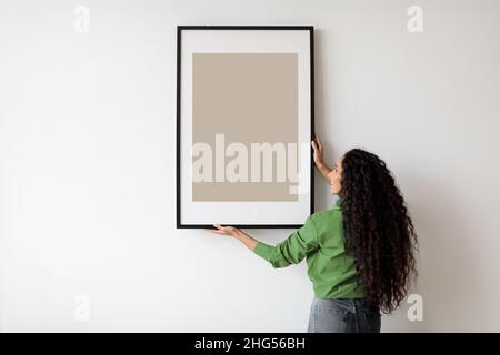 Femme heureuse suspendue affiche vide dans le cadre sur le mur à l'intérieur Banque D'Images