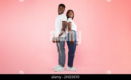 Couple confiant debout dos à dos sur fond rose studio Banque D'Images