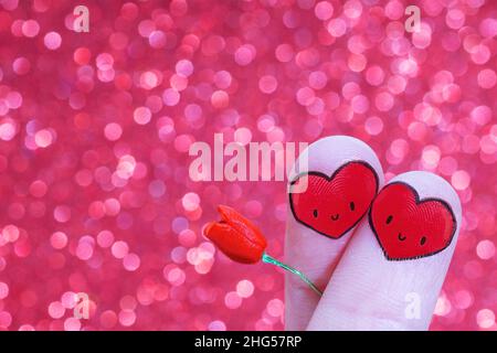 Doigts croisés avec visages souriants en forme de coeur tenant un jouet miniature rose sur un fond bokeh.Concept de date romantique. Banque D'Images