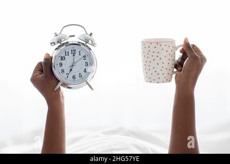 Mains de femme noire non reconnaissables tenant une tasse et une alarme Banque D'Images