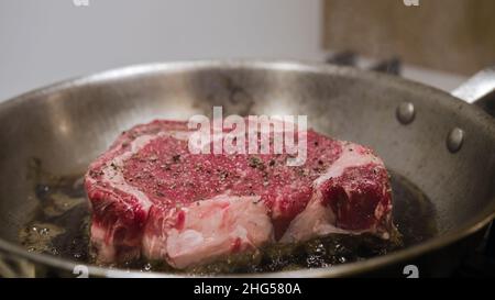 Un steak de bœuf aux yeux juteux, friture à la graisse élevée, dans une poêle.Viande rouge épicée de poivre, gros plan. Banque D'Images