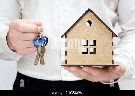 Homme tenant des clés et un modèle miniature de maison en bois dans les mains.Obtenez le concept de la journée des clés. Banque D'Images