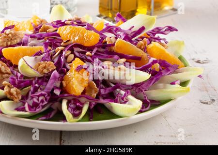 Salade de chou rouge avec endives, fruits orange, pignons de pin grillés et noix sur une table en bois blanc Banque D'Images