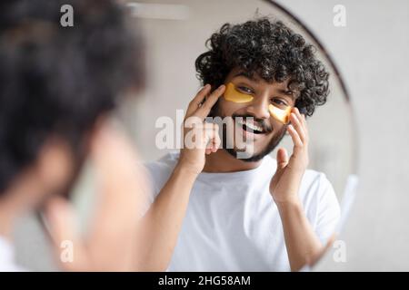 Portrait d'un indien appliquant des cellules oculaires sur son visage et regardant le miroir à la salle de bains Banque D'Images