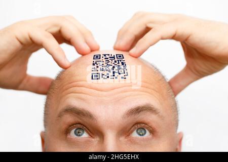 Un homme avec un code qr sur son front. L'homme regarde son code QR sur sa tête. Concept global de maîtrise de la population pour le contrôle et la gouvernance Banque D'Images