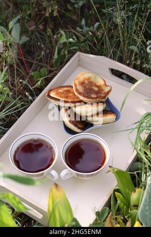 Thé de style campagnard dans le jardin d'été du village.Deux tasses de thé noir chaud et petits gâteaux sur plateau en bois au soleil Banque D'Images