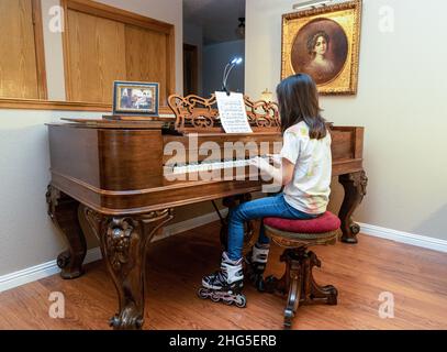 Une jeune fille avec des rollers et un Jean bleu jouant un piano antique et rare Square Grand construit en 1867 avec une peinture antique dans un cadre doré. Banque D'Images