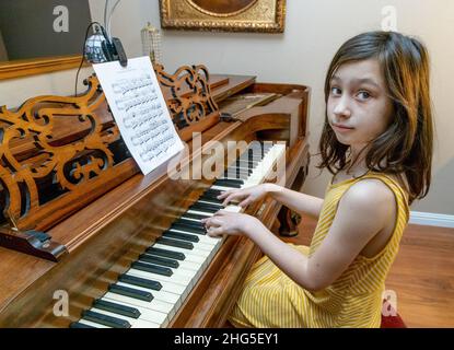 Une jeune fille vêtu d'une robe jaune jouant un rare piano antique Chilling & Sons Square Grand construit en 1867 avec une peinture antique dans un cadre doré. Banque D'Images