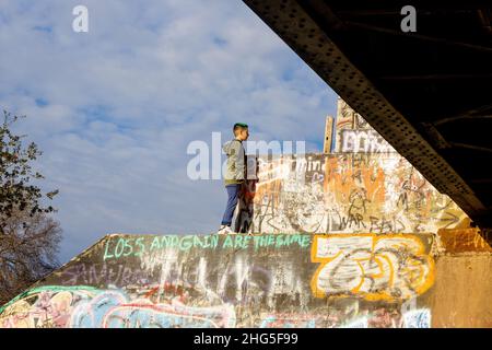 Garçon au-dessus des plates-formes de piliers de chemin de fer à côté d'un pont de train avec graffiti et ciel bleu et nuages Banque D'Images