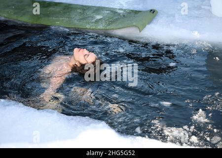 Une jeune femme gracieuse se penchait dans l'eau de glace pendant une baignade en eau froide en hiver au lac Kempenfelt Bay Simcoe Barrie, Ontario Banque D'Images