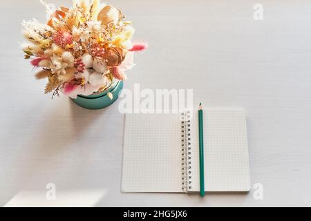 Magnifique bouquet de fleurs séchées, carnet blanc ouvert avec crayon turquoise sur table blanche. Banque D'Images