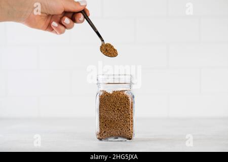 La main d'une femme tient une petite cuillère avec du café instantané sur un pot en verre avec du café. Banque D'Images