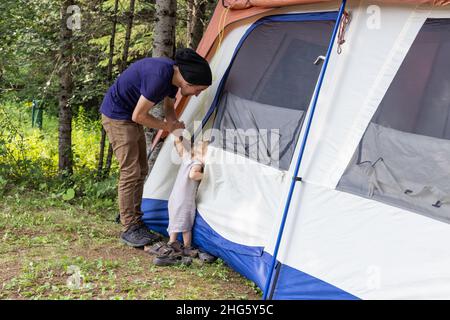 Un jeune père est vu du côté tenant la main d'un garçon de trois ans qui est de piquer la tête dans une grande tente.Papa et son hors réseau camping voyage. Banque D'Images