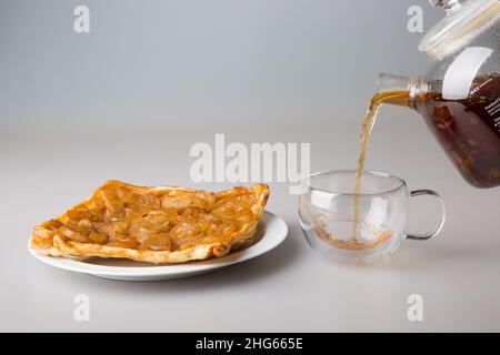 Thé.Un morceau de tarte à la poire dans une soucoupe et une tasse transparente à double paroi.Le thé noir fraîchement préparé est versé dans une tasse à partir d'une théière.Le co Banque D'Images