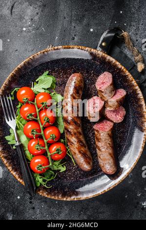 Saucisse bavaroise grillée avec arugula et tomate sur une assiette.Arrière-plan noir.Vue de dessus Banque D'Images