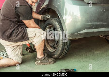 Homme qui se caroupe en mettant une roue d'une voiture dans un atelier Banque D'Images